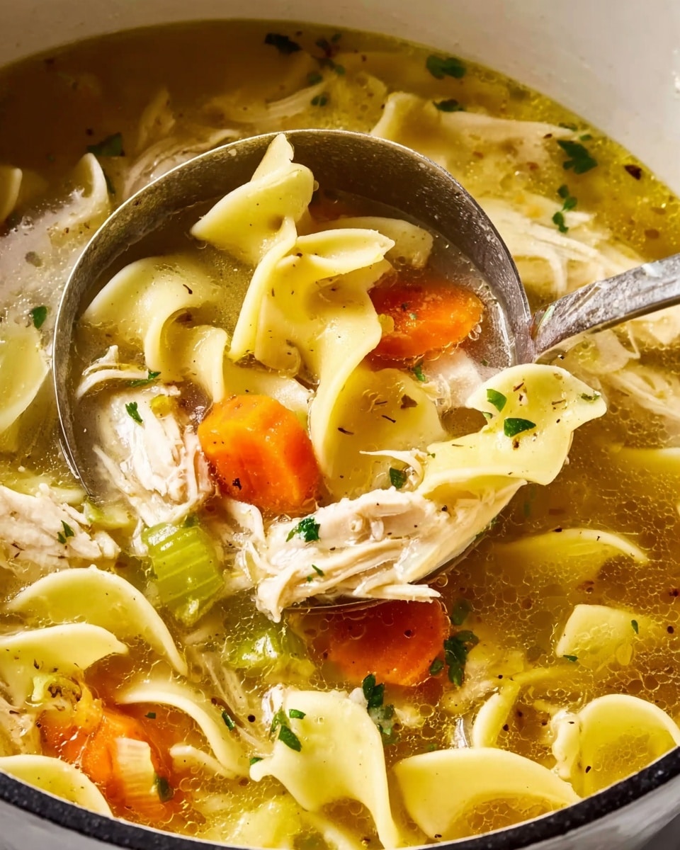 A close-up view of a pot of chicken noodle soup with a large silver ladle scooping some soup. The soup shows wide flat yellow egg noodles folded and floating in a clear golden broth. There are shredded white pieces of chicken layered across the noodles. Bright orange carrot rounds and pale green celery slices add color between the layers. Small flecks of green herbs are sprinkled over the surface. The background is a white marbled texture. Photo taken with an iphone --ar 4:5 --v 7