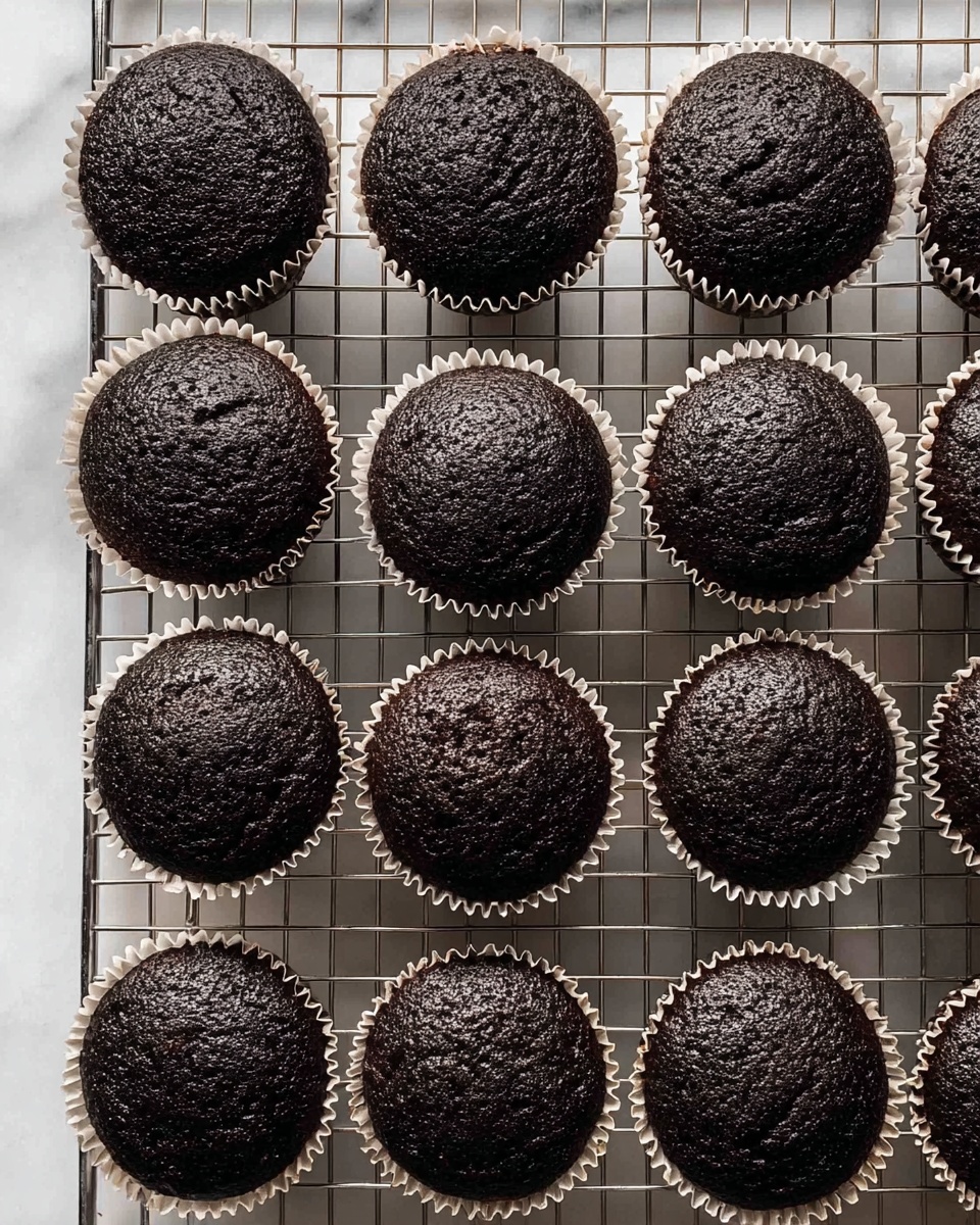 The image shows a close-up top view of fifteen dark chocolate cupcakes in white paper liners arranged neatly on a silver cooling rack. The cupcakes have a slightly rough, matte-textured surface with a rich dark brown color. The rack sits on a white marbled surface, which adds a clean and bright background, making the cupcakes stand out. The cupcakes are evenly spaced in rows, filling the frame with no other objects visible. photo taken with an iphone --ar 4:5 --v 7