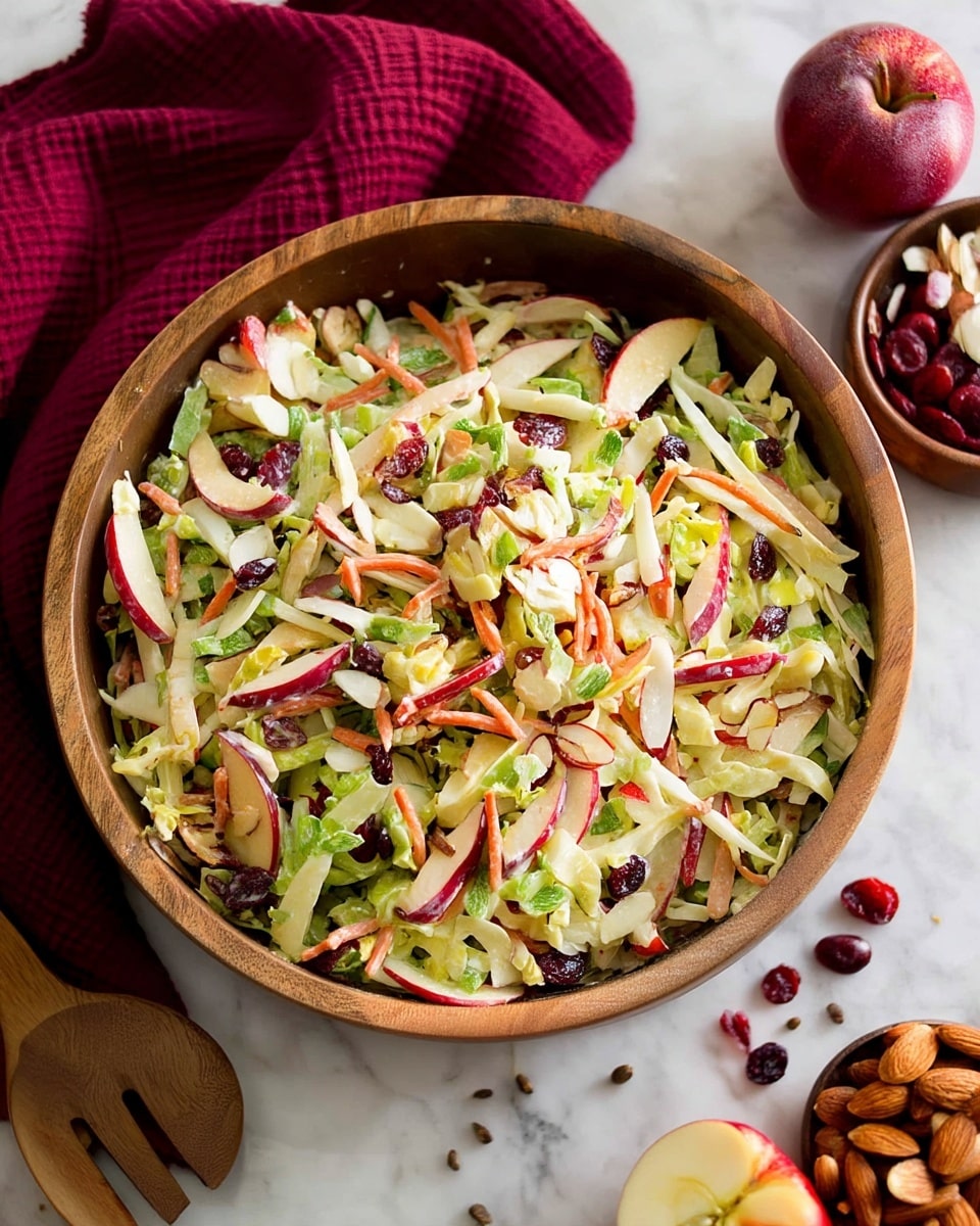 The image shows a wooden bowl filled with a fresh salad made of several layers: the bottom layer is light green shredded cabbage mixed with small bright green pieces of scallions. On top of this, there are thin orange carrot strips, thin red apple slices with skin, and scattered dark red dried cranberries. There are also white sliced almonds mixed throughout the salad, adding texture. The wooden bowl sits on a white marbled surface. photo taken with an iphone --ar 4:5 --v 7