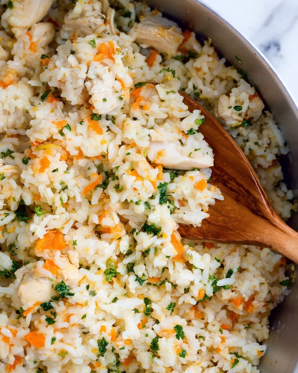 The image shows a close-up of a dish with mixed cooked rice that is white and soft in texture, with small pieces of orange carrots and green herbs spread all over. There are also small, white pieces of tender chicken mixed in the rice. The dish is being stirred or scooped with a wooden spoon on the right side, revealing a mix of grains and ingredients. The background has a white marbled texture. Photo taken with an iphone --ar 4:5 --v 7
