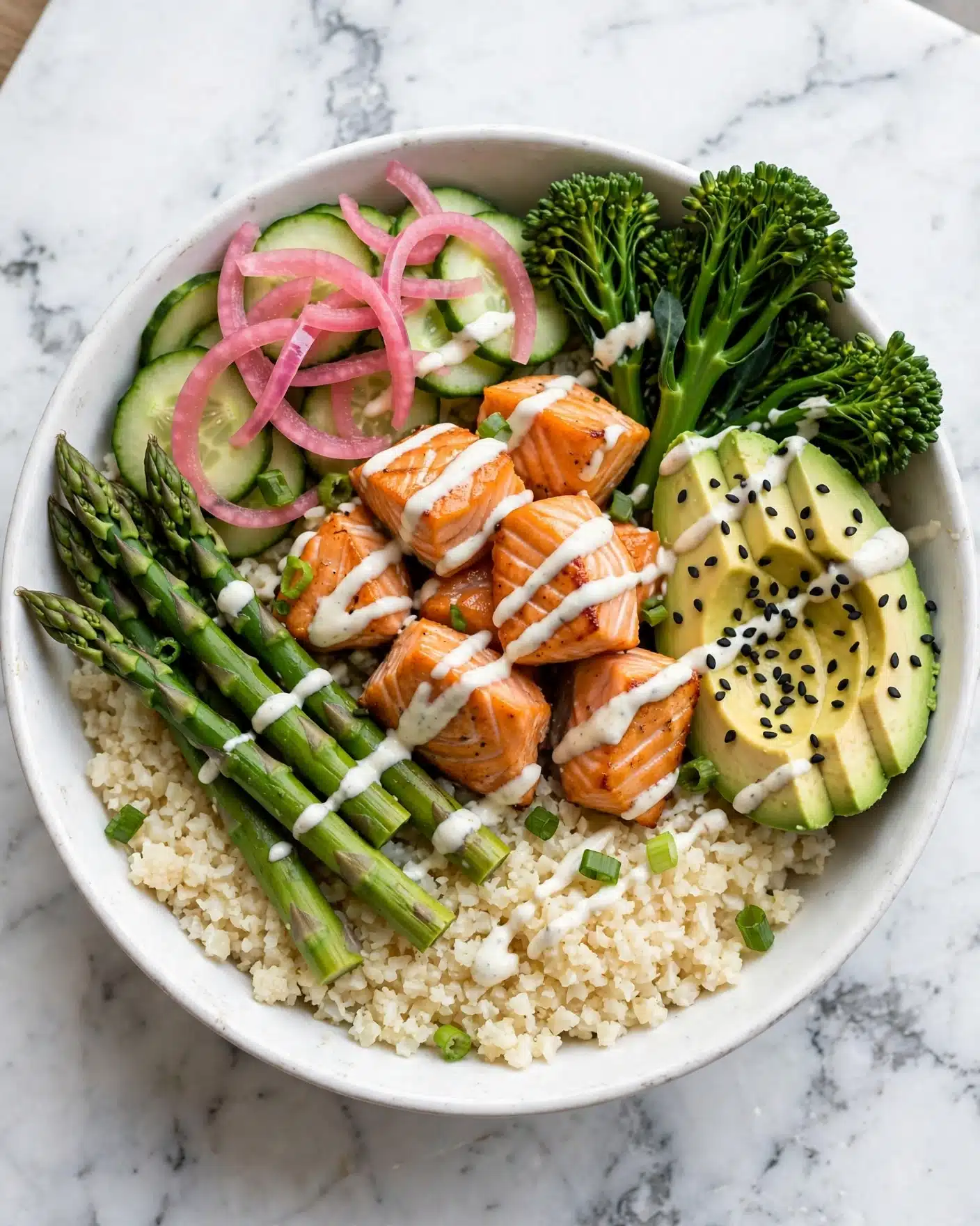 A white bowl filled with six layers: at the bottom, a layer of light beige cauliflower rice with a fluffy texture; above it, bright green asparagus spears laid on the left side; next to them, chunks of orange grilled salmon in the middle, some drizzled with white sauce; on the top left, thin light green cucumber slices partly covered by pink pickled onions; on the right side, slices of creamy light green avocado sprinkled with black sesame seeds; and near the top right, bunches of vibrant green broccolini. The dish is garnished with small green onion pieces and a light white sauce drizzle scattered throughout, all set on a white marbled surface. photo taken with an iphone --ar 4:5 --v 7