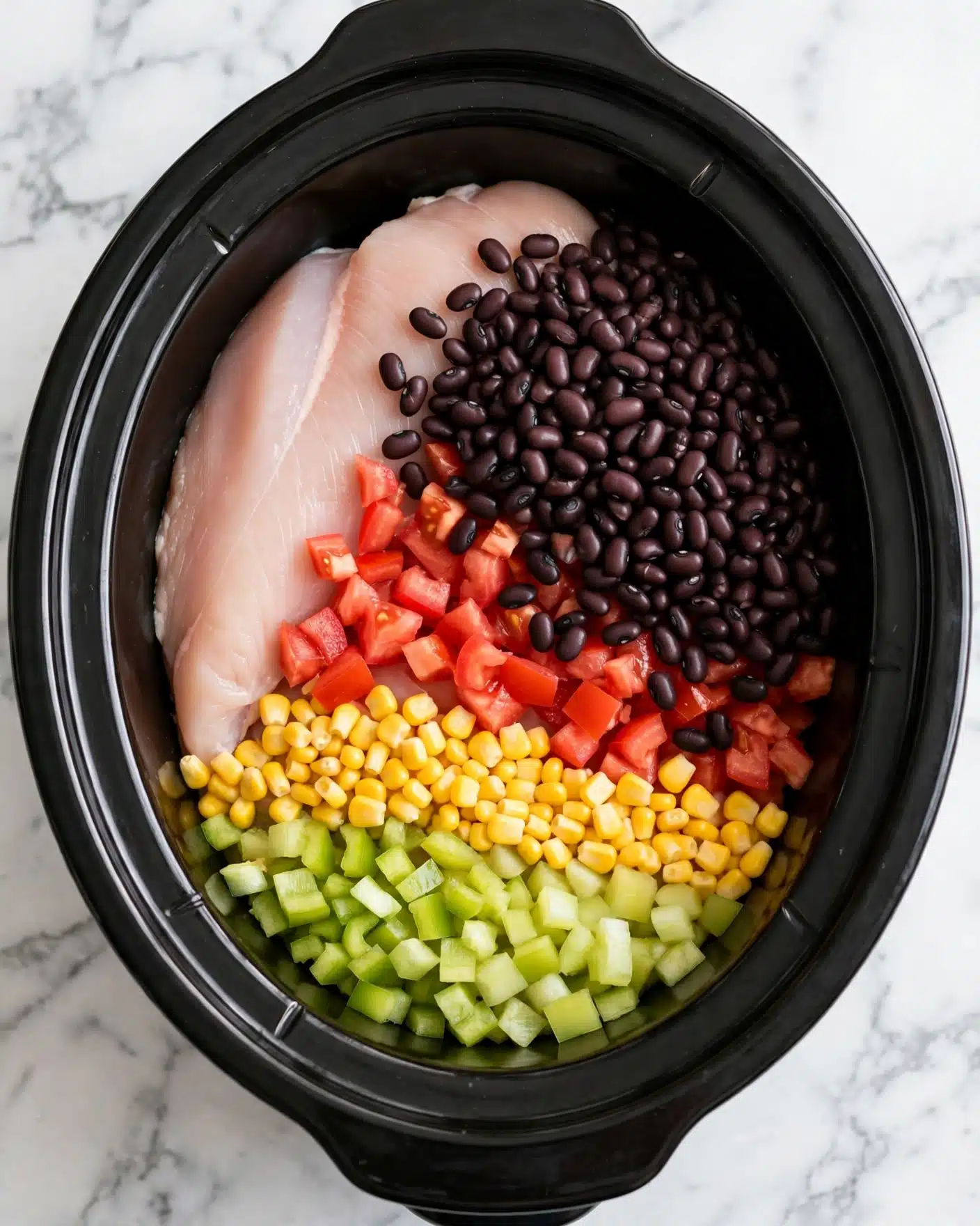 The image shows a black slow cooker filled with layered ingredients. At the bottom, a large, smooth, pale pink piece of chicken lies slightly curved along the pot. On top of the chicken, black beans spread in a thick line, mainly on the right side. Below the beans, bright red diced tomatoes are scattered, adding contrast. Beneath the tomatoes, yellow corn kernels form a neat row toward the front. In front of the corn, pale green chopped peppers cover the area closest to the bottom edge. The slow cooker sits on a white marbled surface. Photo taken with an iphone --ar 4:5 --v 7