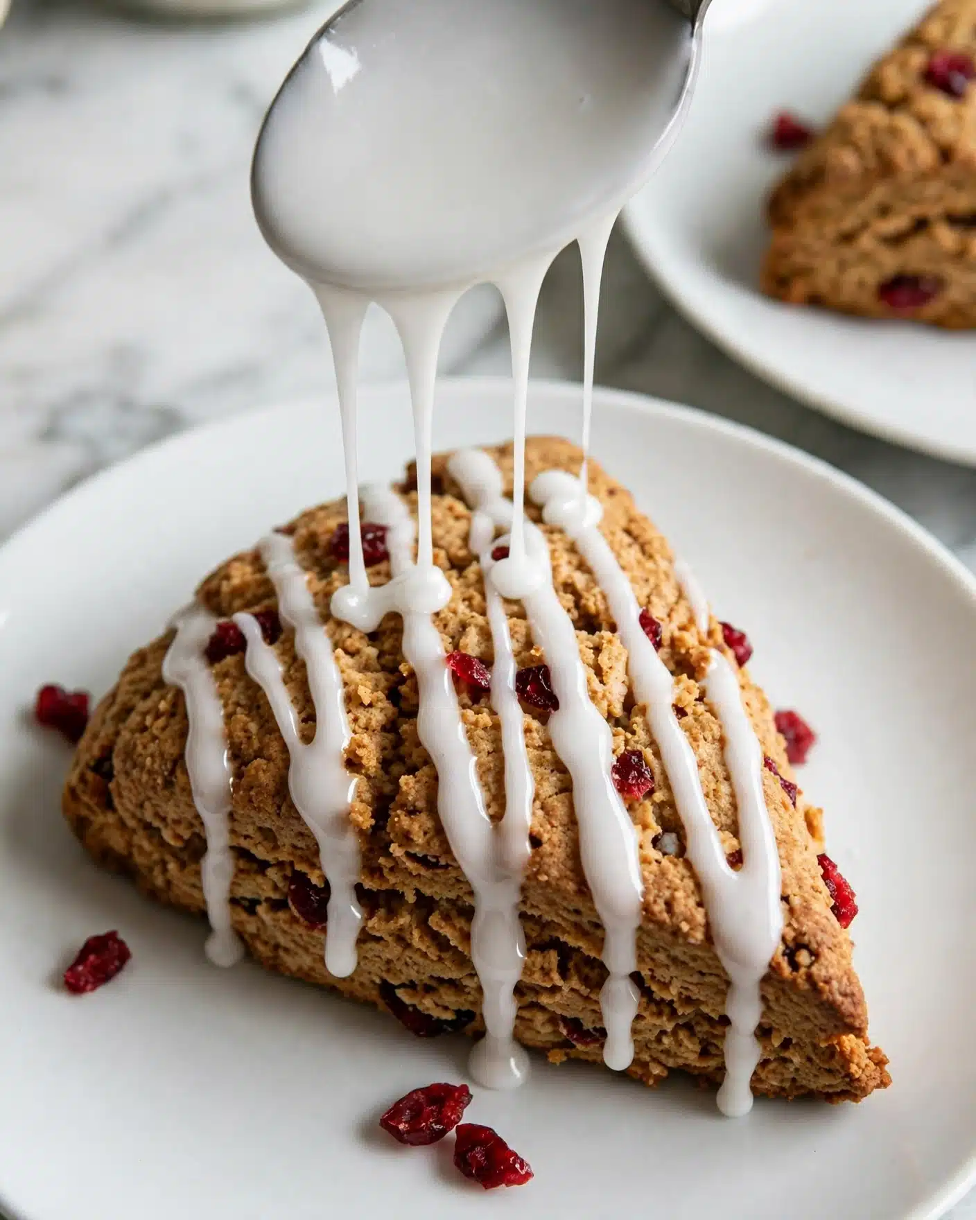 Classic Homemade Pastry Scones with Mix-ins and Glaze Recipe 6 The image shows four golden brown scones with a crumbly texture, each triangular in shape, arranged closely on a wire cooling rack. The scones have visible dried red cranberries scattered throughout their surface, adding bright red spots. White icing drizzle is spread in parallel lines across the top of each scone, contrasting with their warm tones. The wire rack is placed on a white marbled surface with a few loose dried cranberries scattered around, and a portion of a white bowl is slightly visible in the corner. The scene has bright lighting, highlighting the scones' texture and the shiny icing. Photo taken with an iphone --ar 4:5 --v 7