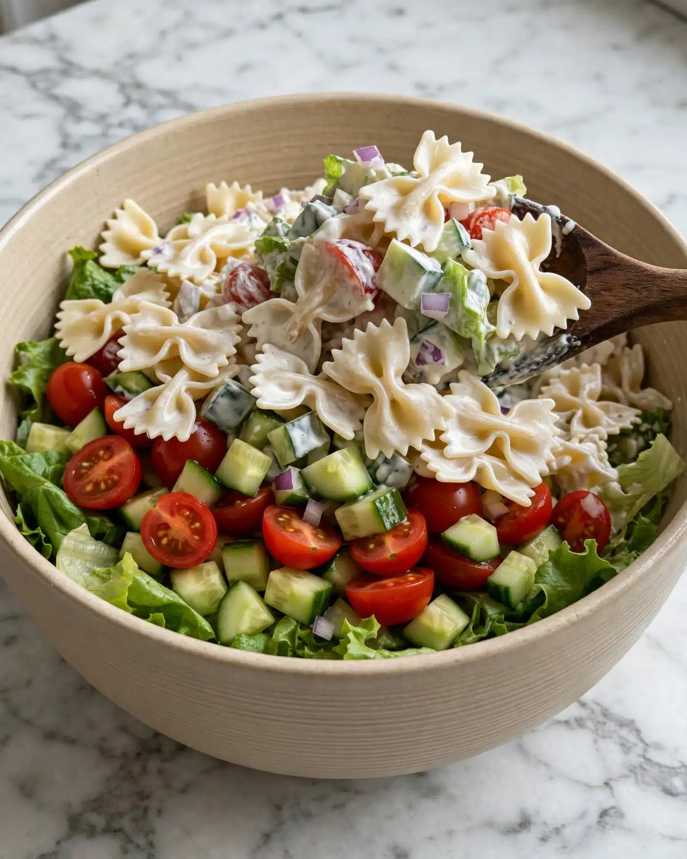 A white plate holds a layered salad starting with a base of fresh green lettuce leaves. On top of the lettuce is a layer of golden-brown, crispy bowtie-shaped pasta pieces that look crunchy and seasoned with black pepper. Small diced cucumber pieces sit to one side, adding a fresh green color, while red cherry tomato halves peek through under the pasta on the other side. A thick, creamy white sauce with a hint of herbs generously covers the pasta layer in uneven streaks. The whole scene is set against a white marbled textured surface. photo taken with an iphone --ar 4:5 --v 7