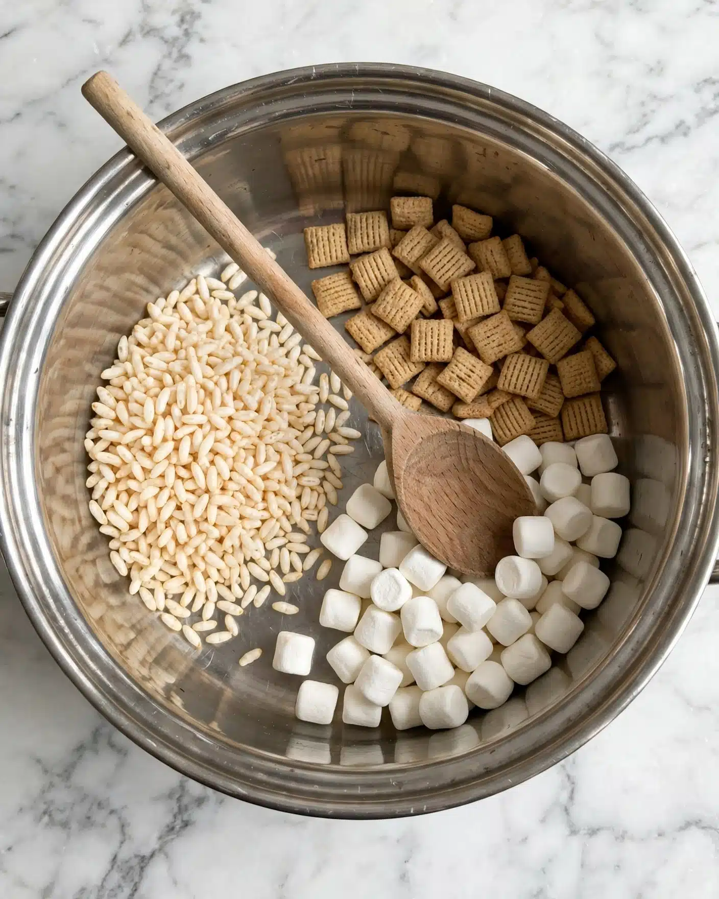A silver pot containing three separate groups of ingredients: pale beige puffed rice on the left, small white marshmallows on the bottom right, and light brown square cereal pieces on the top right, with a wooden spoon resting inside the pot on the marshmallows. The pot is placed on a white marbled surface. photo taken with an iphone --ar 4:5 --v 7
